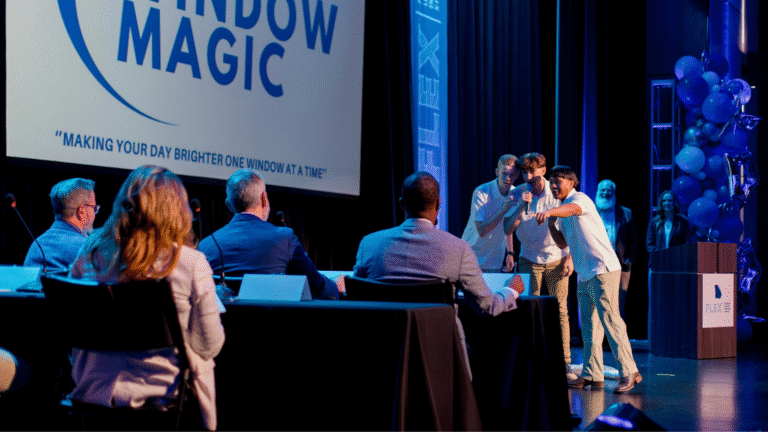 Three student entrepreneurs enthusiastically present their business idea, “Window Magic,” to a panel of Georgia judges during a pitch competition, with balloons, a podium, and event branding in the background.
